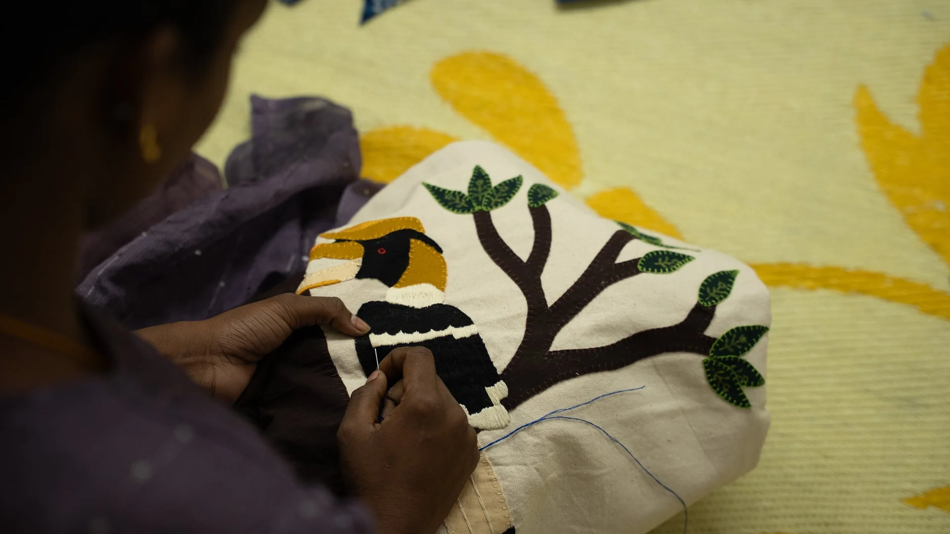 An Urumala artisan hand-stitching a hornbill motif on a story cushion cover